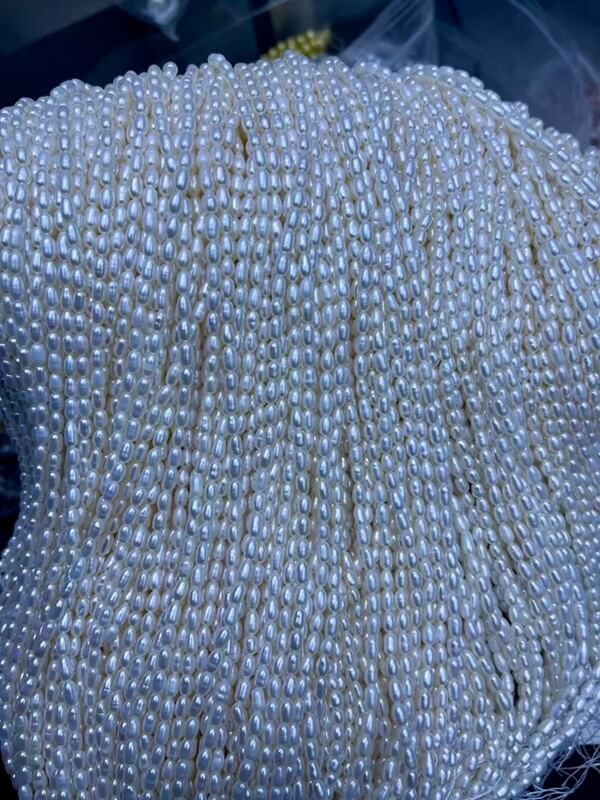 Wholesale 3mm white rice freshwater pearl strands held in hand, high-quality cultured pearls bulk supplies for independent jewelry designers and studios.