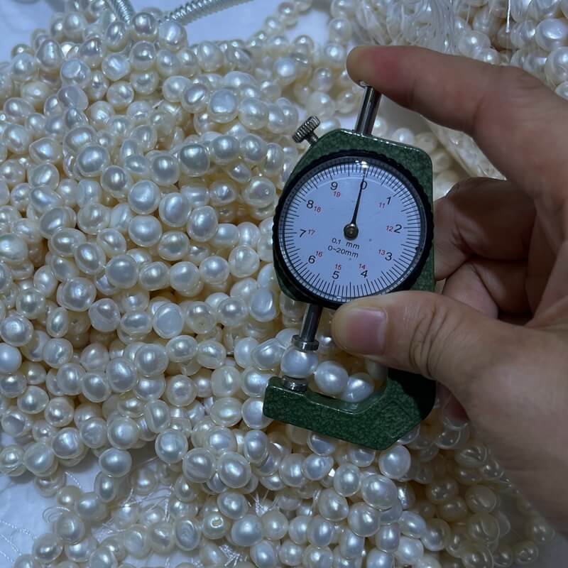 Measuring 10-11mm irregular cultured baroque pearls with a caliper for quality control.