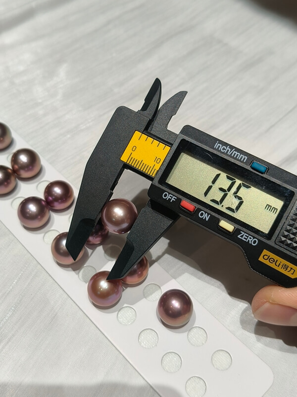 Digital caliper measuring a large 13.5mm deep purple Edison pearl with high mirror luster.