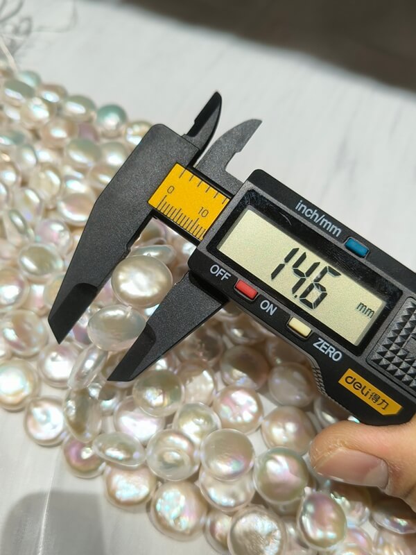 A caliper showing a 14.6mm diameter measurement on metallic rainbow luster disc pearl strands.