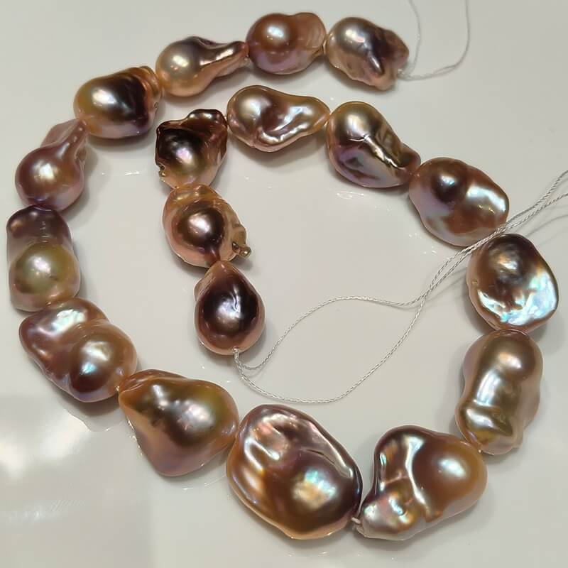 A single 16-inch strand of natural purple and pink freshwater baroque pearls arranged on a white background.