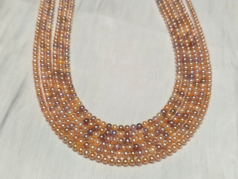 Five wholesale strands of premium baby pearls showcasing a lustrous mix of natural champagne, lavender, and peach tones.