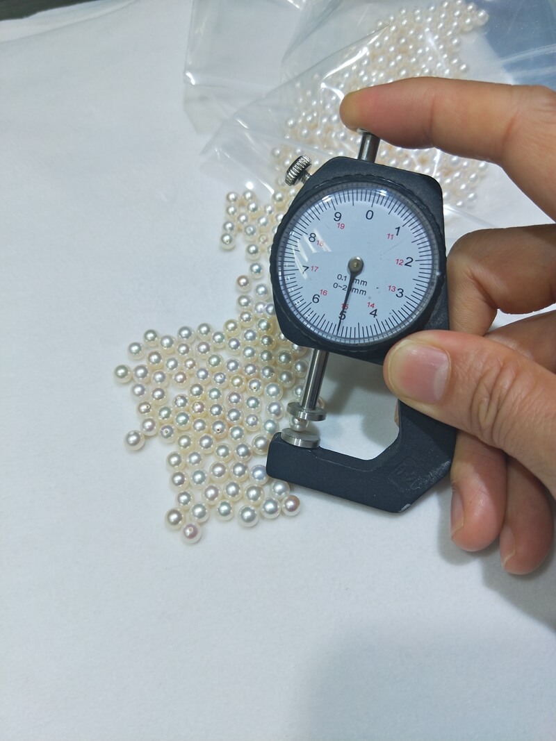 A dial caliper measuring a perfectly round 5mm half-drilled freshwater pearl. High-precision matched pearls wholesale, tailored specifically for the gold-standard size of everyday stud earrings pearl designs.