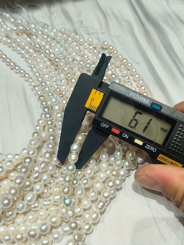 Measuring a 6.1mm nugget baroque pearl strand with a digital gauge, high-quality cultured material for personalized pearl necklace making.