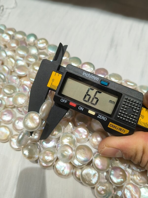 Digital caliper measuring the 6.6mm thickness of high luster wholesale coin baroque pearls.
