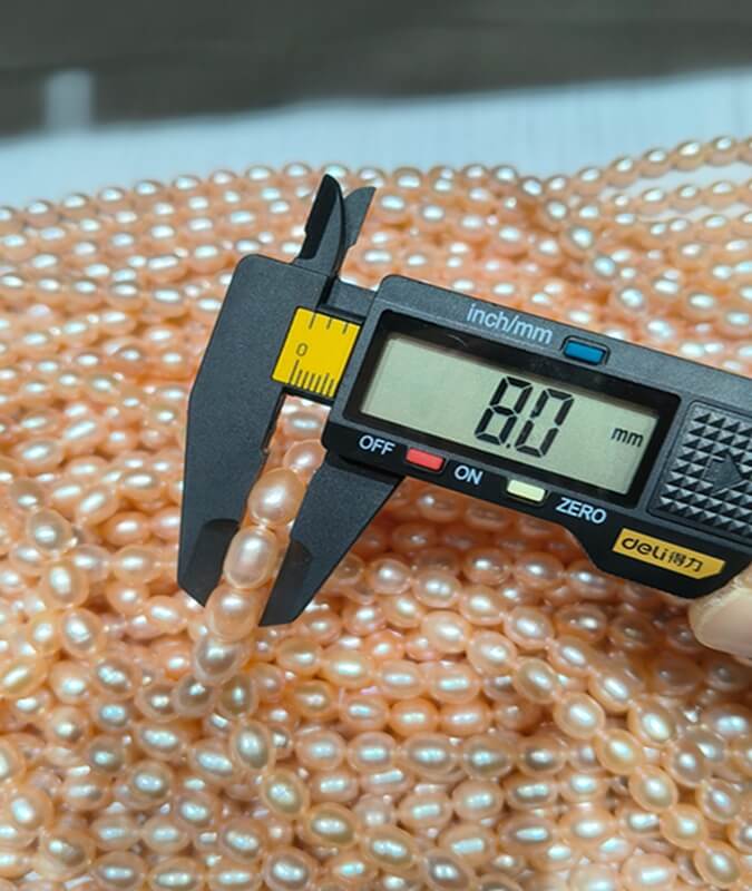 Caliper measuring an 8.0mm natural peach pink freshwater oval pearl strand for wholesale supply