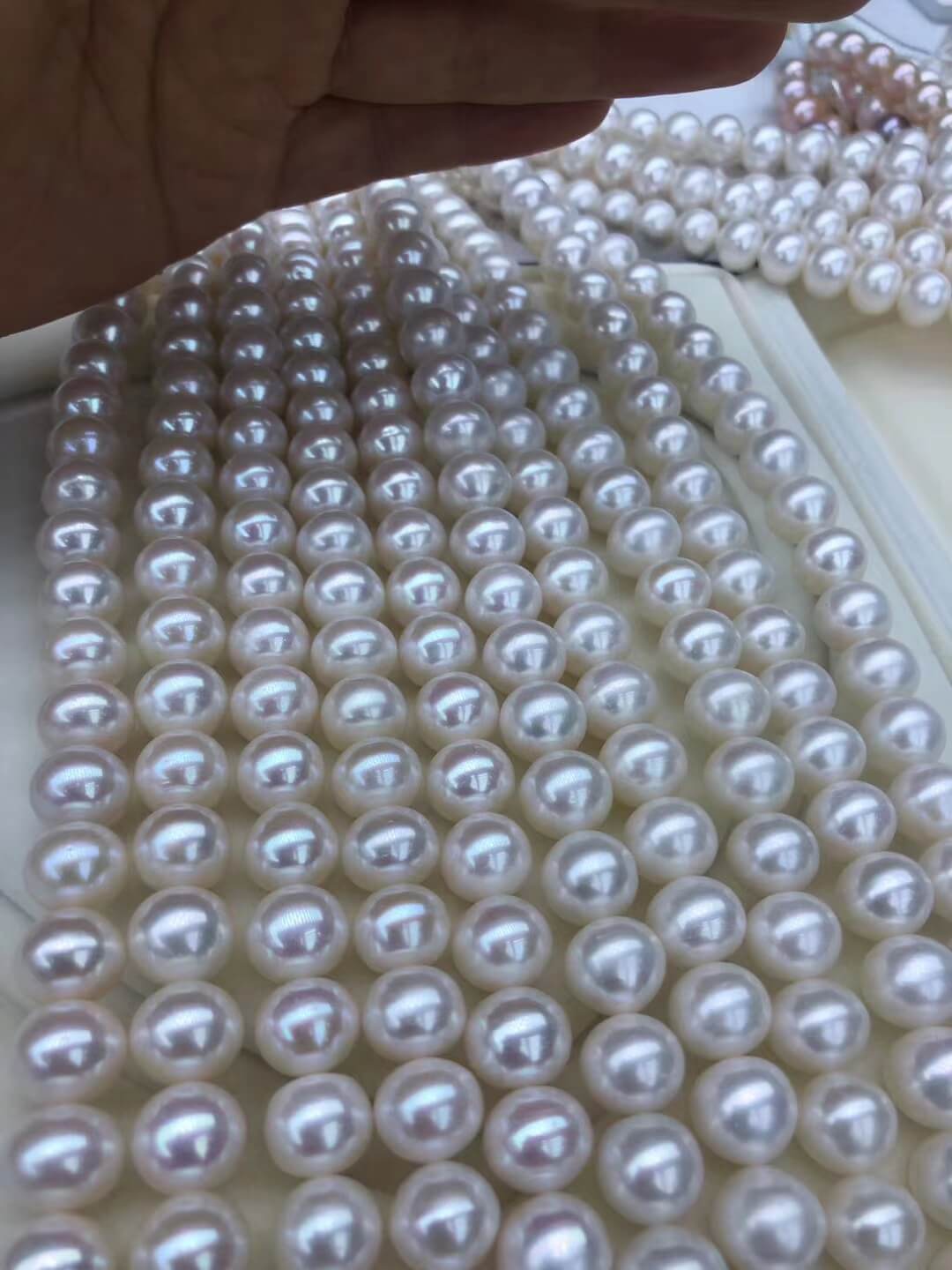 A bulk lot of 9-10mm high luster white freshwater pearl beads in loose strands for jewelry making.
