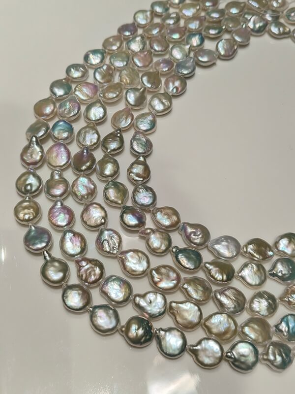 Close-up of flat round baroque coin pearls in bulk showcasing smooth surfaces and mirror-like pink-green orient.