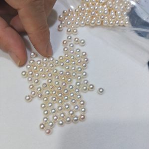 Close-up of a hand sorting loose 5mm round freshwater pearls. Half-drilled, high-luster pearl supplies ideal for boutique jewelers crafting elegant stud earrings pearl collections.