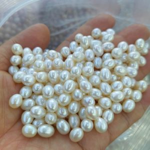A hand holding a cluster of loose white rice pearls with bright watery luster. Ideal lightweight bulk pearl supplies for artisan jewelers creating elegant pearl earrings dangle collections.
