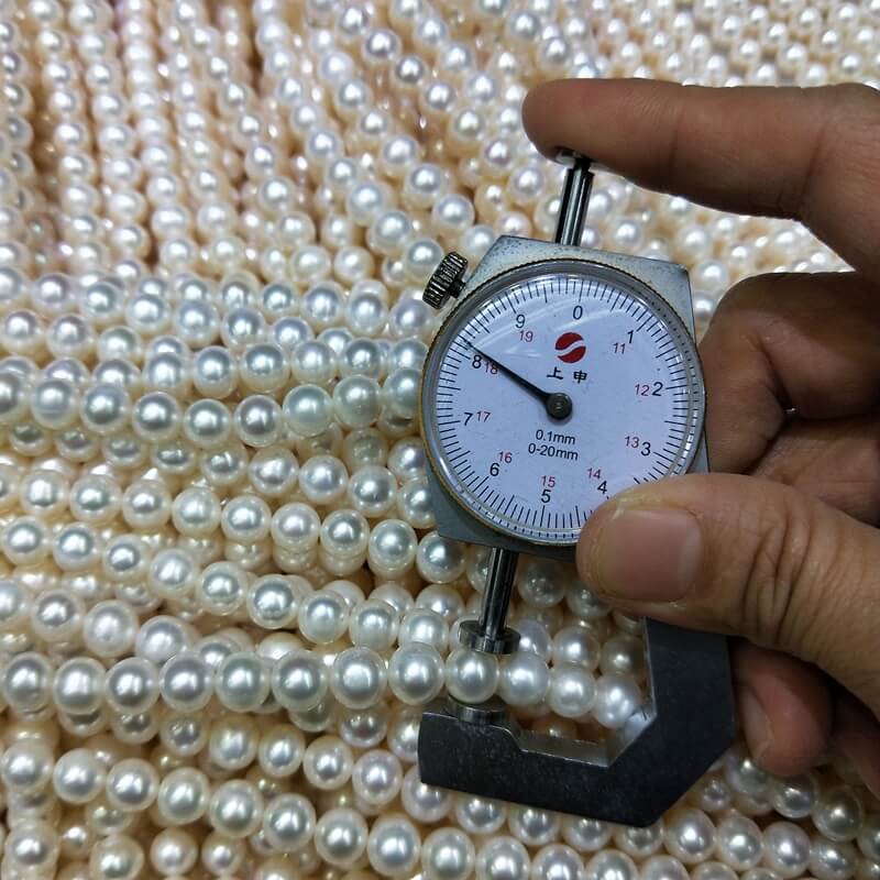 Close-up of a digital caliper measuring the uniform 8mm size of white near-round freshwater pearls on a 16-inch bulk loose bead strand.