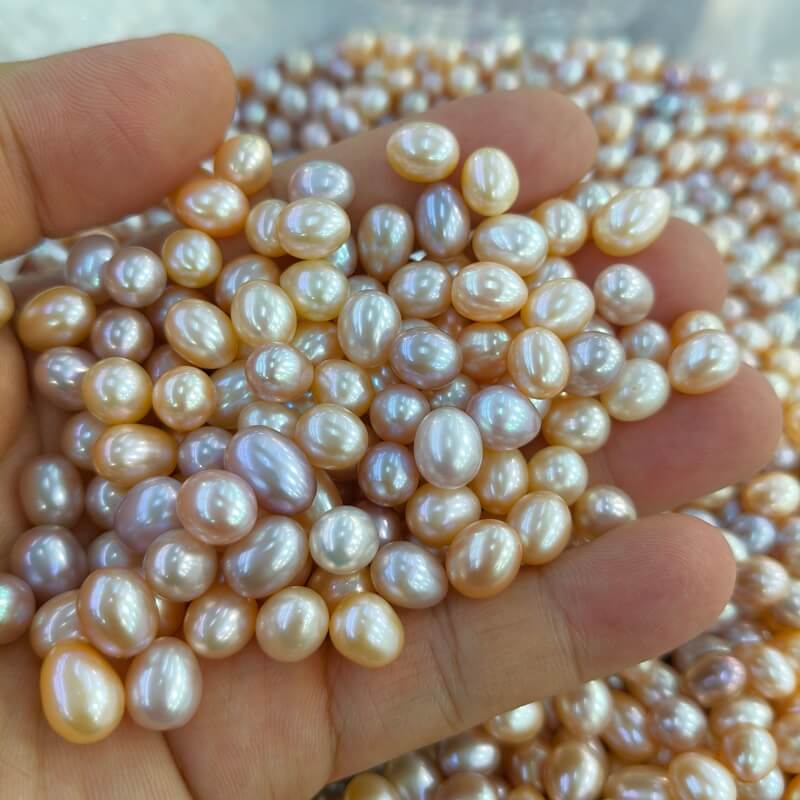 A handful of mixed natural color freshwater rice pearls in shades of peach, lavender, and cream. High-luster loose pearls perfect for custom baroque pearl earrings dangle designs.