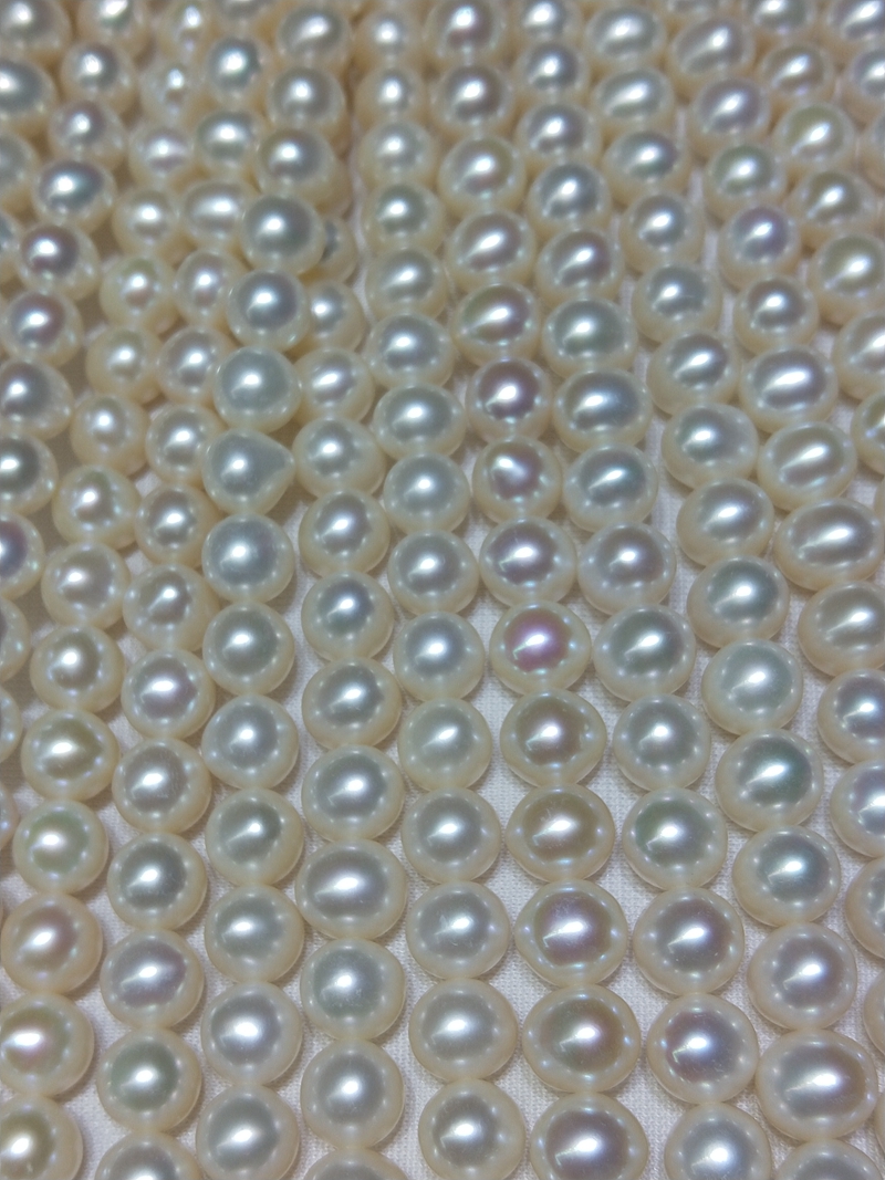 Close-up of fully drilled 9-10mm potato freshwater pearl strands showing precise 0.7-0.8mm hole size for jewelry wire threading.