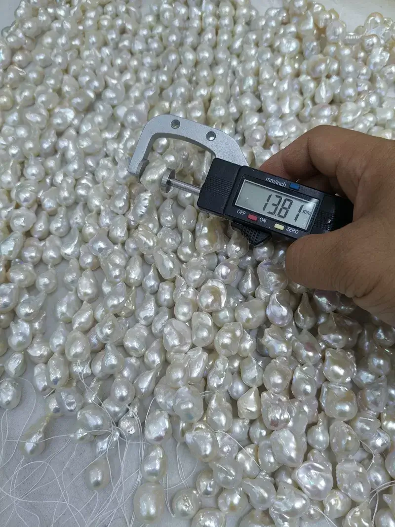 Close up of a 13.81mm freshwater flame baroque pearl strand measured by a digital caliper, displaying premium grade loose pearls with metallic orient for jewelry designers.