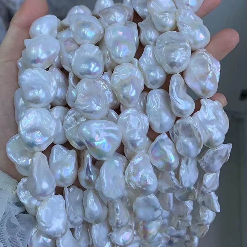 A hand holding large 16-inch wholesale chunky white baroque pearl strands with high luster, perfect for creating designer pearl necklaces.