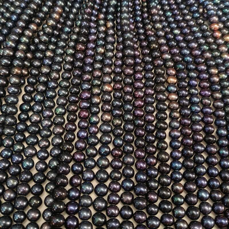 Factory quality control process measuring cultured black pearls with a dial thickness gauge to ensure precise 9-10mm caliber sizing.