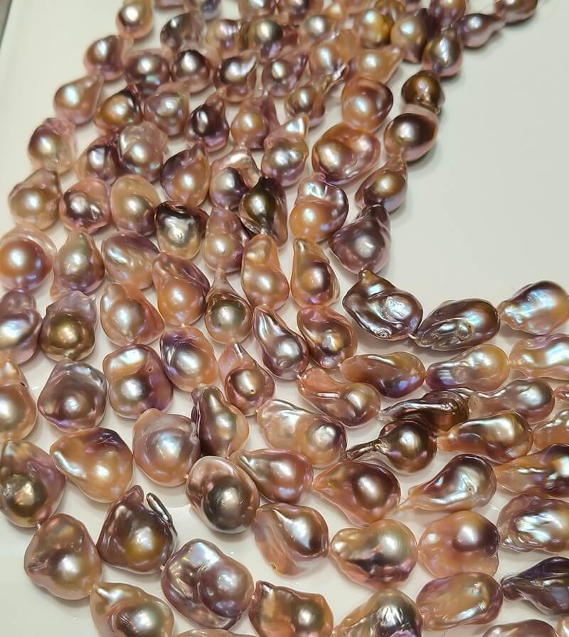 A bundle of wholesale purple and pink baroque pearl strands with intense metallic luster, ideal for designer jewelry making.